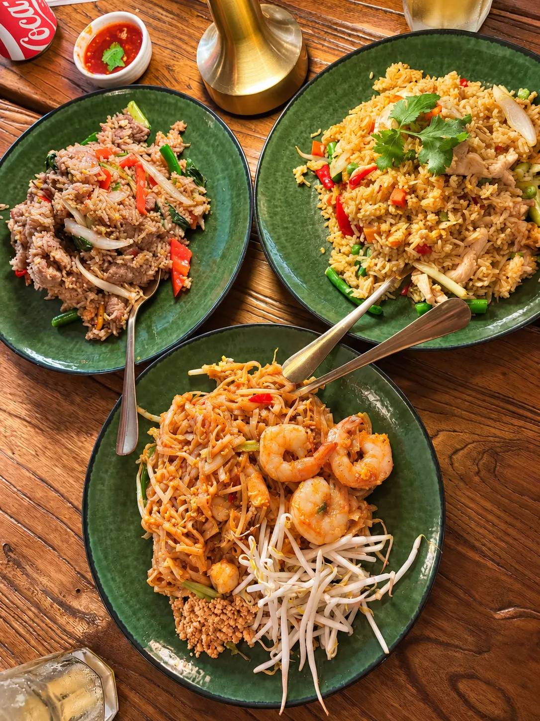 Three green plates: beef fried rice, chicken fried rice with cilantro, and shrimp pad thai with bean sprouts and peanuts.