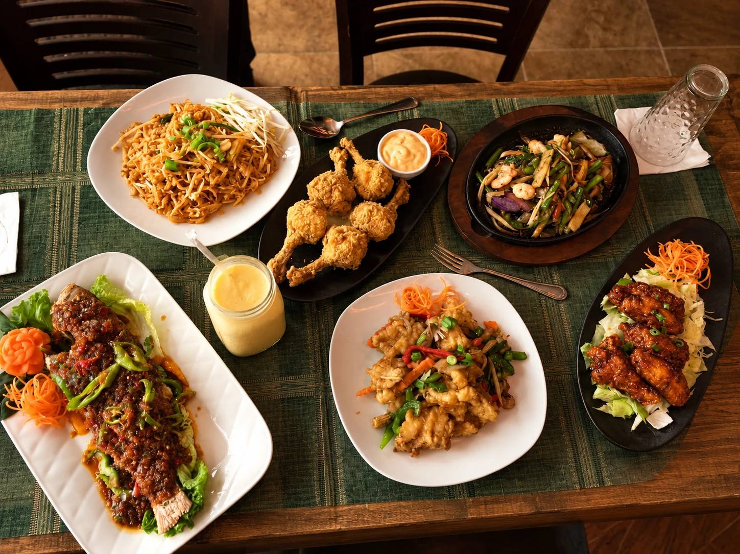 Overhead table of dishes: pad thai, fried chicken, shrimp stir-fry, whole fish in chili sauce, fried calamari and glazed wings.